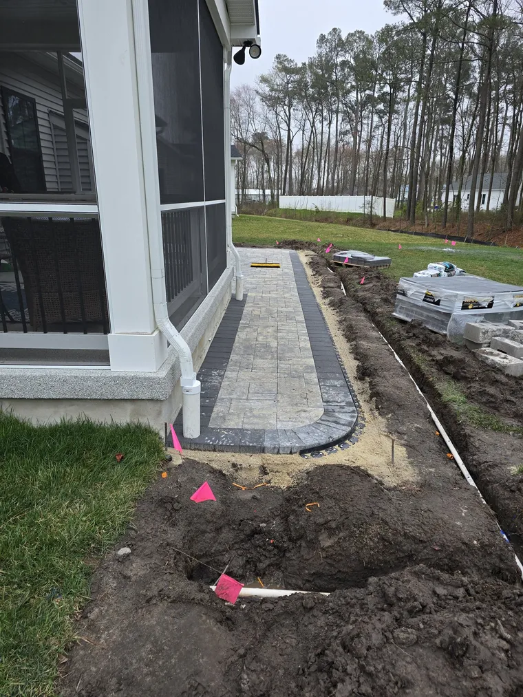 Underground downspout drain trench alongside a new paver walkway